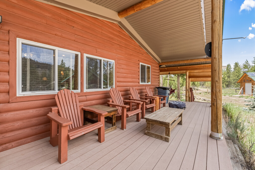 Covered porch at Bonanza Cabin with outdoor seating surrounded by pine trees.