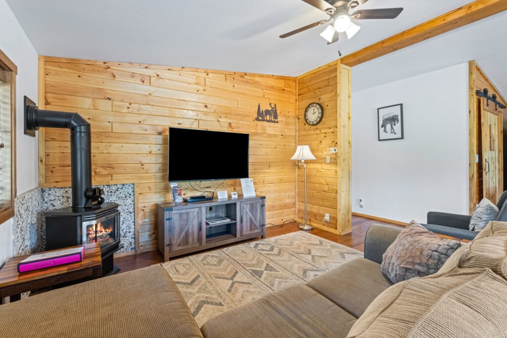 Bonanza Cabin living room with gas stove, TV, wood accent wall and sectional sofa.