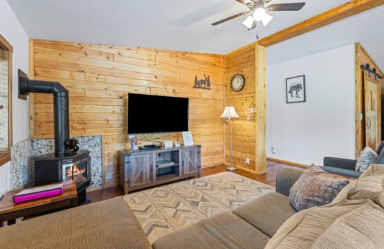 Bonanza Cabin living room with gas stove, TV, wood accent wall and sectional sofa.
