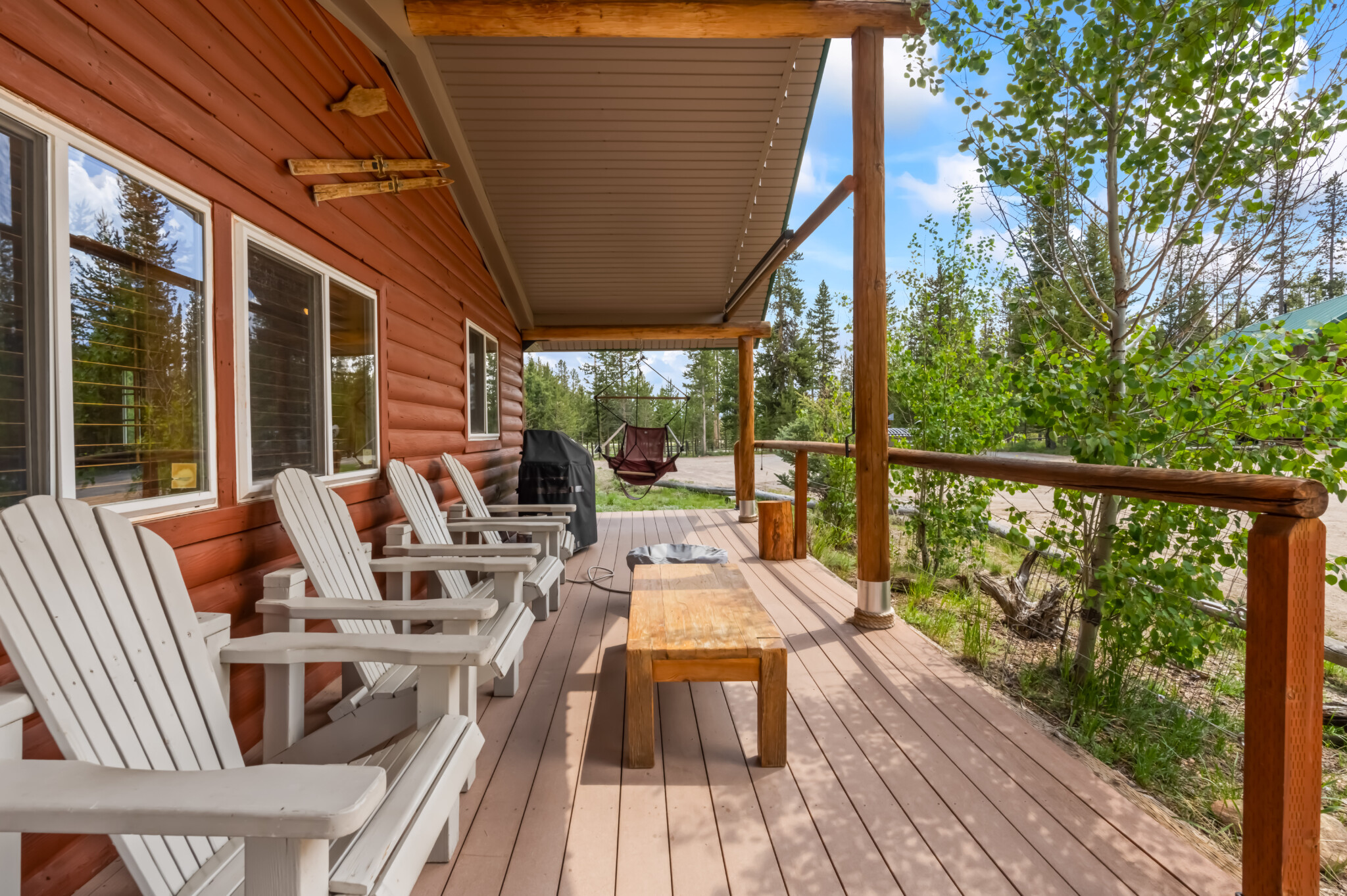 Covered porch at Valley Creek Cabin with Adirondack chairs and wooded views.